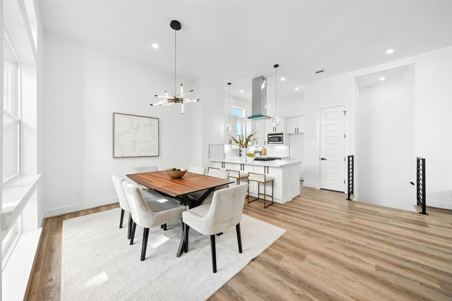 Bright and spacious dining area with an open-concept layout, featuring high ceilings, wide-plank wood flooring, and large windows that bring in abundant natural light. The space flows seamlessly into the modern kitchen, complete with Quartz countertops, a waterfall island, custom cabinetry, and designer lighting Bright and spacious dining area with an open-concept layout, featuring high ceilings, wide-plank wood flooring, and large windows that bring in abundant natural light. The space flows seamlessly into the modern kitchen, complete with Quartz countertops, a waterfall island, custom cabinetry, and designer lighting