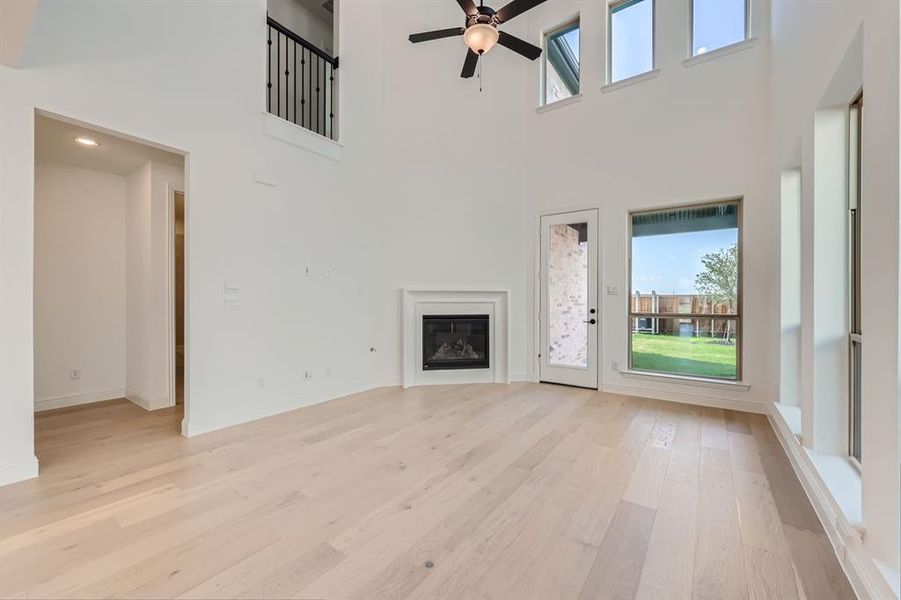 Unfurnished living room with ceiling fan, light wood-type flooring, and a high ceiling