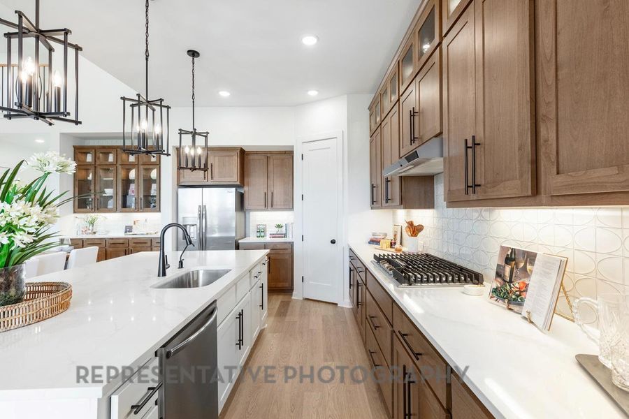 Kitchen featuring stainless steel appliances, under cabinet range hood, a sink, a notable chandelier, and brown cabinets
