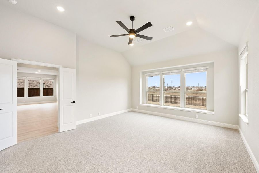 Empty bedroom with vaulted ceiling, ceiling fan, carpet flooring, and large windows overlooking a backyard Empty bedroom with vaulted ceiling, ceiling fan, carpet flooring, and large windows overlooking a backyard