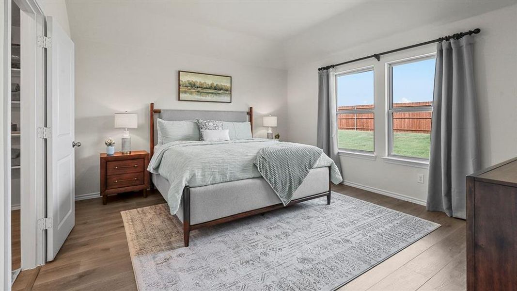 This bedroom features light wood-style flooring, white walls, and two windows offering views of the exterior yard
