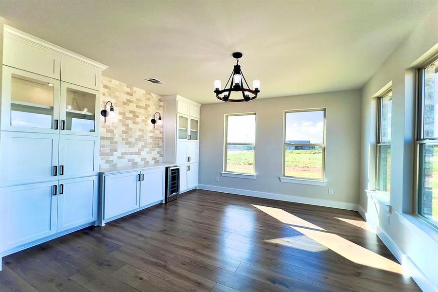Dining area with healthy amount of natural light, dark flooring, a chandelier, and beverage cooler