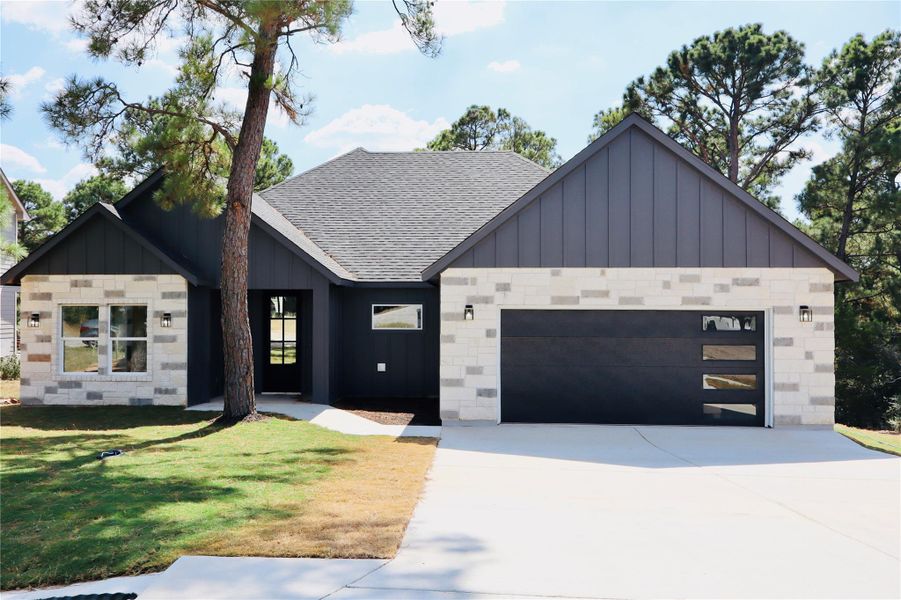 Modern farmhouse with board and batten siding, roof with shingles, concrete driveway, an attached garage, and stone siding