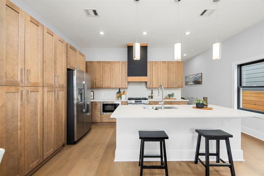 The kitchen is a chef’s dream, complete with sleek quartz countertops, modern pendant lighting, stainless steel appliances, and warm wood cabinetry.