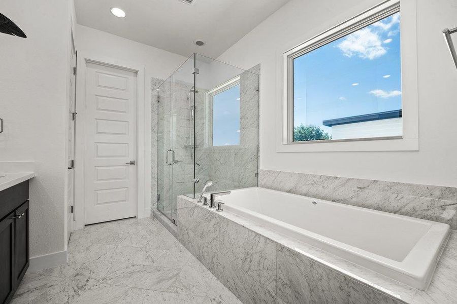 Soaking tub framed by stunning Carrara marble surrounds, oversized windows, and serene natural light for a spa-like retreat.