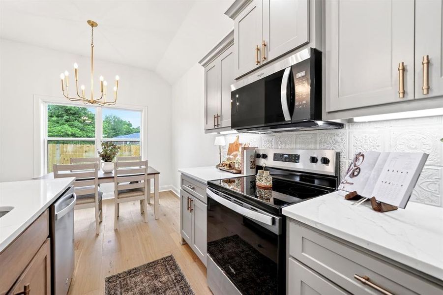 Contemporary kitchen featuring light wood-finish flooring, white countertops, and gray cabinetry with gold-tone hardware