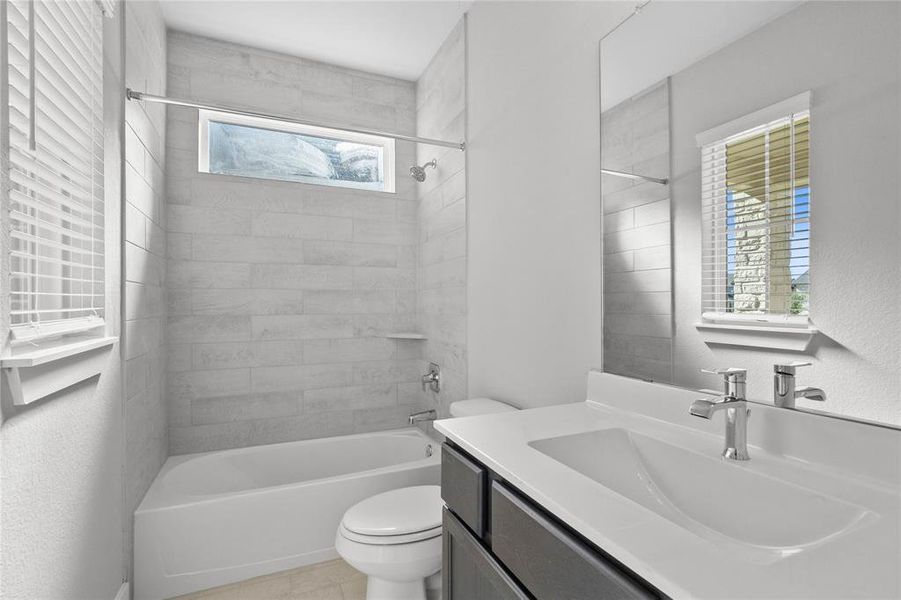 Secondary bath features tile flooring, bath/shower combo with tile surround, wood stained cabinets, beautiful light countertops, mirror, dark, sleek fixtures and modern finishes!