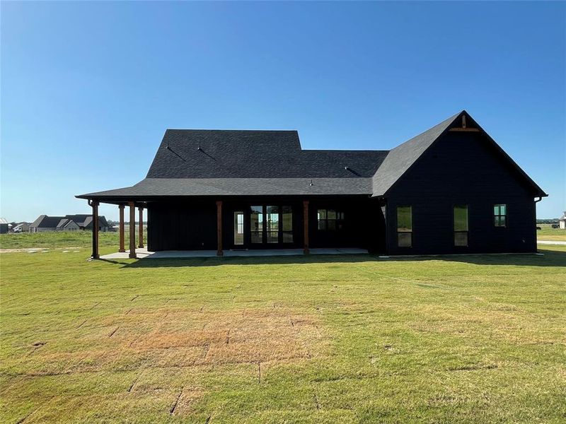 Contemporary home exterior featuring dark siding, a dark shingle roof, and a covered patio with wood columns