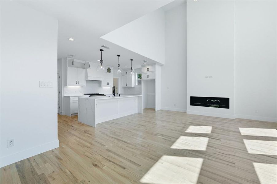 Unfurnished living room with light wood-type flooring, recessed lighting, and a towering ceiling