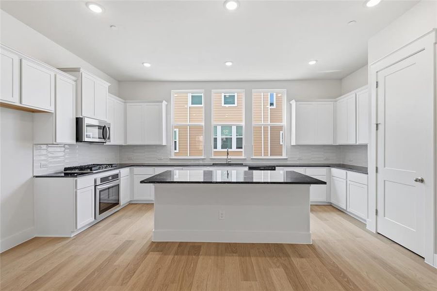 This kitchen boasts light wood flooring, white cabinetry, dark countertops, and stainless steel appliances