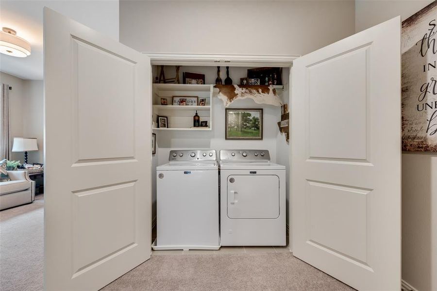 Laundry closet featuring a built-in washer and gas dryer, upper shelving for storage, and white panel doors Laundry closet featuring a built-in washer and gas dryer, upper shelving for storage, and white panel doors