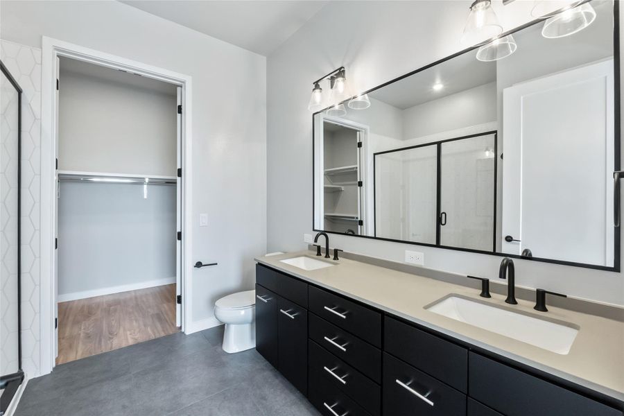 Bathroom with a walk in closet, a stall shower, double vanity, and tile patterned floors