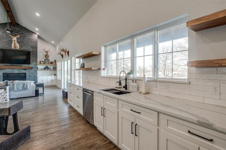 Kitchen with sink, light stone counters, tasteful backsplash, dishwasher, and white cabinets