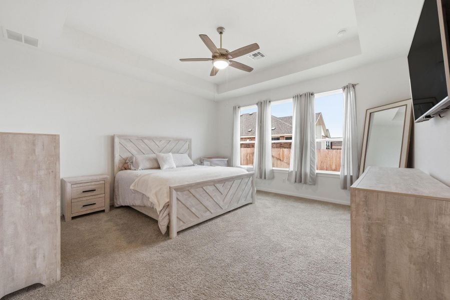 Bedroom featuring a tray ceiling, a ceiling fan, and light carpet