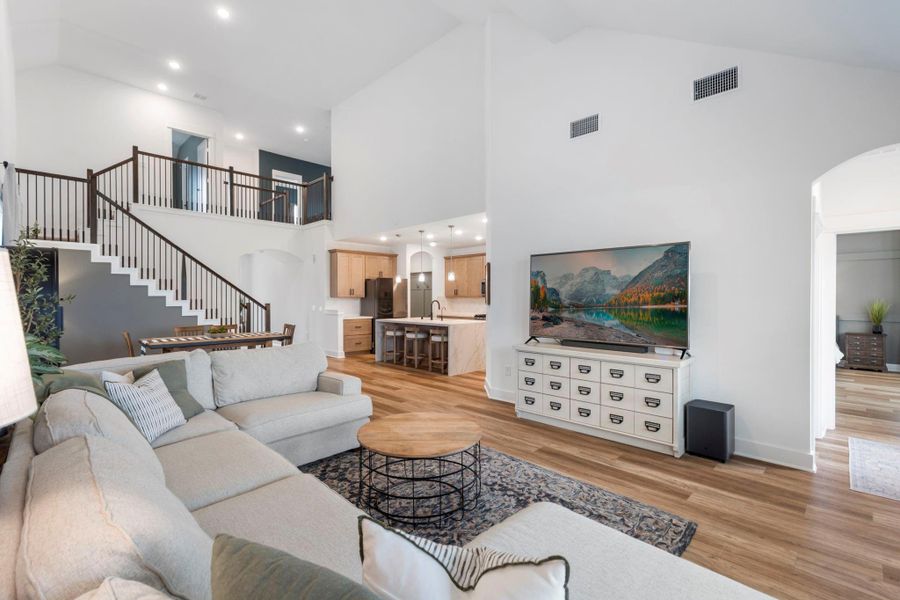 This spacious living area features high ceilings and an open layout, with a cozy sectional sofa, large TV, and modern kitchen with a breakfast bar. The elegant staircase leads to an upper level, adding to the home's inviting atmosphere. This spacious living area features high ceilings and an open layout, with a cozy sectional sofa, large TV, and modern kitchen with a breakfast bar. The elegant staircase leads to an upper level, adding to the home's inviting atmosphere.