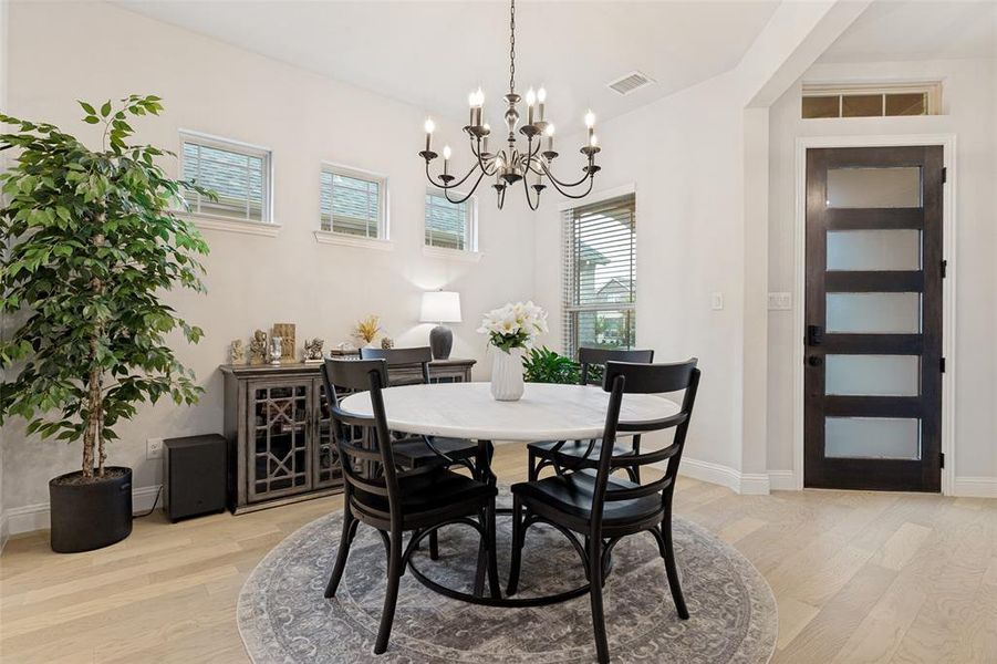 Dining space featuring wood-finish flooring, a contemporary dark wood door with frosted glass panels, and an overhead chandelier