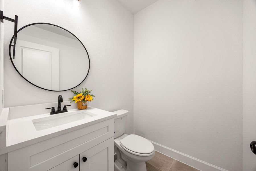 Stylish powder room showcasing a sleek white vanity with solid surface countertop, black hardware, and a round statement mirror. Bright, modern, and thoughtfully designed for everyday convenience and guests.