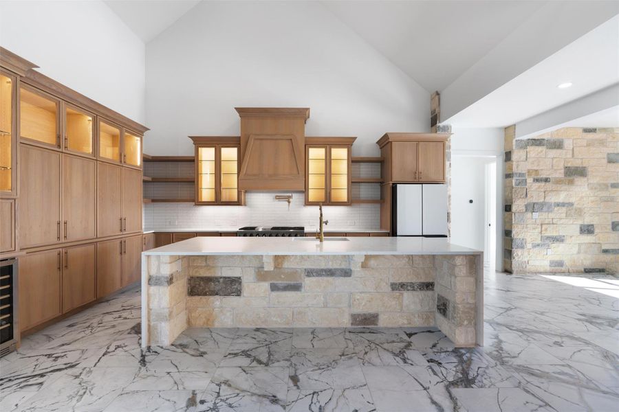 Kitchen with open shelves, glass insert cabinets, high vaulted ceiling, freestanding refrigerator, and light marble finish flooring