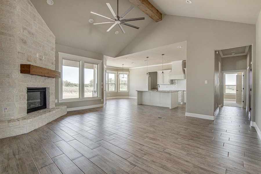 Unfurnished living room with light wood-type flooring, a fireplace, beamed ceiling, high vaulted ceiling, and ceiling fan