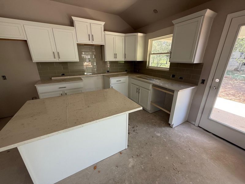 Kitchen featuring decorative backsplash, a kitchen island, vaulted ceiling, white cabinets, and light stone counters