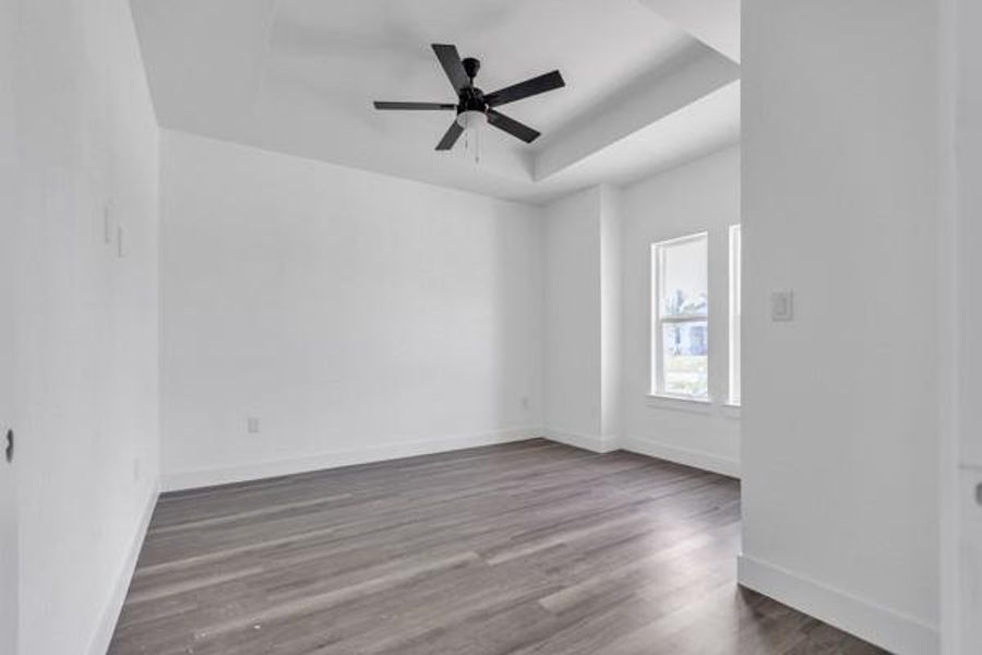 Spare room with a tray ceiling, dark wood-type flooring, and a ceiling fan