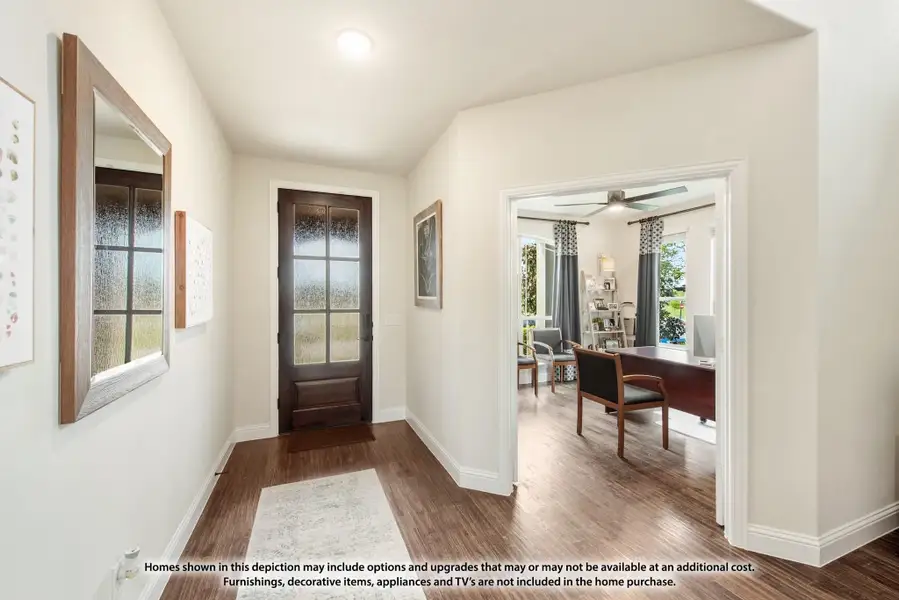 Entryway with dark wood front door, hardwood floors, and view into a home office with ceiling fan