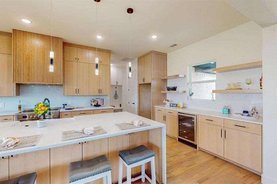 Kitchen with light wood-type flooring, stainless steel range, wine cooler, hanging light fixtures, and a breakfast bar