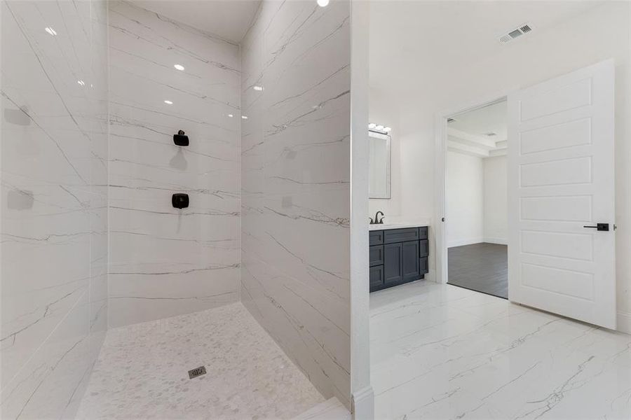Contemporary bathroom featuring a spacious walk-in shower with full height tile surround and pebble tile flooring, a dark-toned vanity with an integrated sink, and white tile flooring Contemporary bathroom featuring a spacious walk-in shower with full height tile surround and pebble tile flooring, a dark-toned vanity with an integrated sink, and white tile flooring