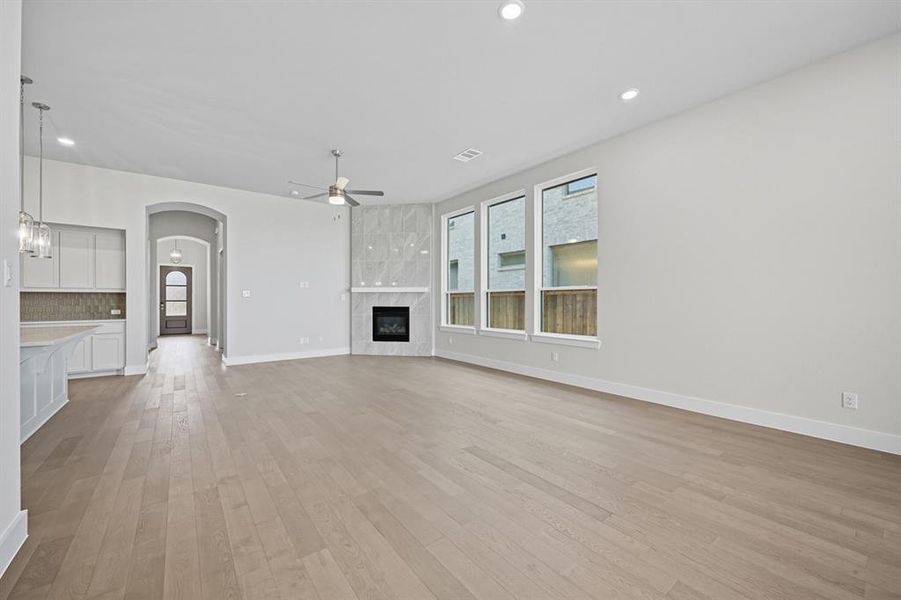 Unfurnished living room featuring light wood-style flooring, a fireplace, arched walkways, recessed lighting, and a ceiling fan Unfurnished living room featuring light wood-style flooring, a fireplace, arched walkways, recessed lighting, and a ceiling fan