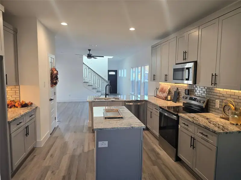 Kitchen featuring backsplash, appliances with stainless steel finishes, gray cabinets, a peninsula, and light stone counters Kitchen featuring backsplash, appliances with stainless steel finishes, gray cabinets, a peninsula, and light stone counters
