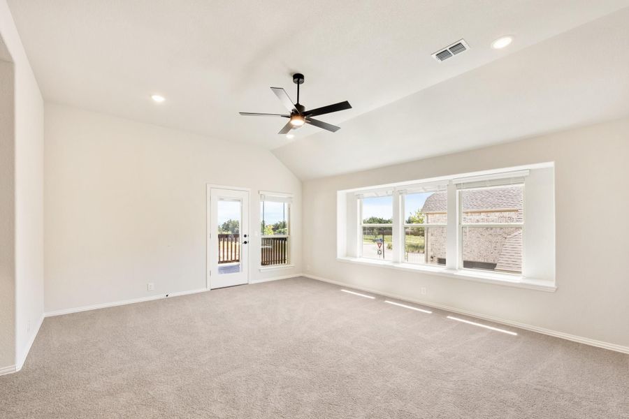 Empty living room with vaulted ceiling, ceiling fan, carpet, large windows, and glass door to patio Empty living room with vaulted ceiling, ceiling fan, carpet, large windows, and glass door to patio