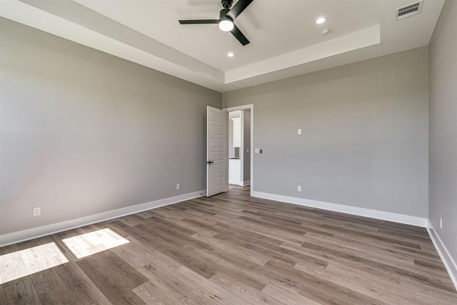 Spare room featuring ceiling fan, light wood-type flooring, and a tray ceiling