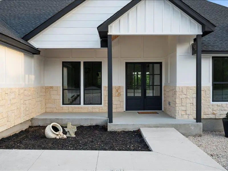 Exterior showcasing white siding, stone accents, black-framed windows, and a black double entry door
