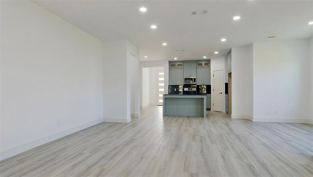 Kitchen featuring open floor plan, dark countertops, glass fronted cabinets, recessed lighting, and a center island with sink