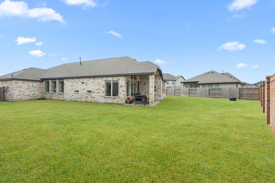 The backyard offers a spacious lawn with full fencing and no immediate rear neighbors visible from the covered patio. Grass has been digitally enhanced for marketing purposes.