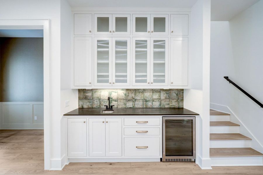 Thoughtfully designed entertaining spaces continue beyond the kitchen with this custom built beverage bar featuring glass front cabinetry, under counter wine fridge, designer tile backsplash, and elevated finishes throughout. A perfect blend of style and function that showcases Harvard Homes’ attention to detail. *Previous Project*