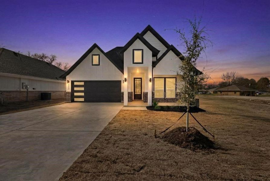 View of front facade featuring driveway, stone siding, an attached garage, and board and batten siding