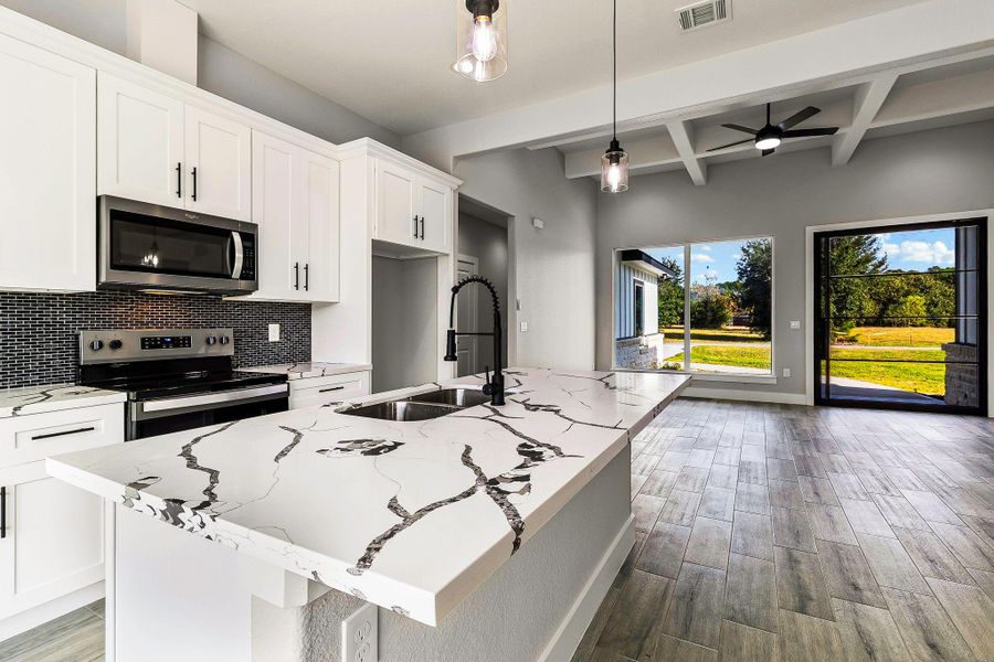 This modern kitchen boasts sleek white cabinetry, a stylish marbled countertop, and stainless steel appliances. An open layout leads to a spacious living area with large windows and a view of the backyard, offering plenty of natural light. This modern kitchen boasts sleek white cabinetry, a stylish marbled countertop, and stainless steel appliances. An open layout leads to a spacious living area with large windows and a view of the backyard, offering plenty of natural light.