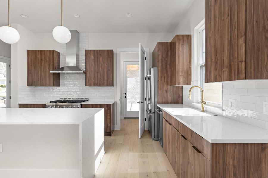 Kitchen featuring high end fridge, a sink, light countertops, wall chimney range hood, and modern cabinets