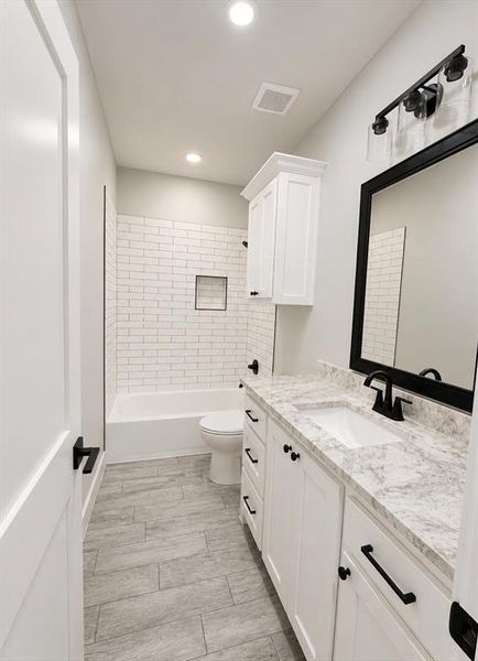 Bathroom featuring a white subway tile shower surround with a built-in niche, a white vanity with slab countertop, a rectangular undermount sink, and black fixtures Bathroom featuring a white subway tile shower surround with a built-in niche, a white vanity with slab countertop, a rectangular undermount sink, and black fixtures