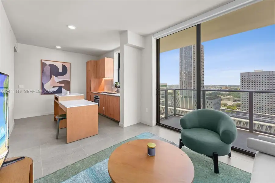 Floor-to-ceiling windows, private balcony, wood-finish cabinetry, built-in kitchen island, and neutral tile flooring