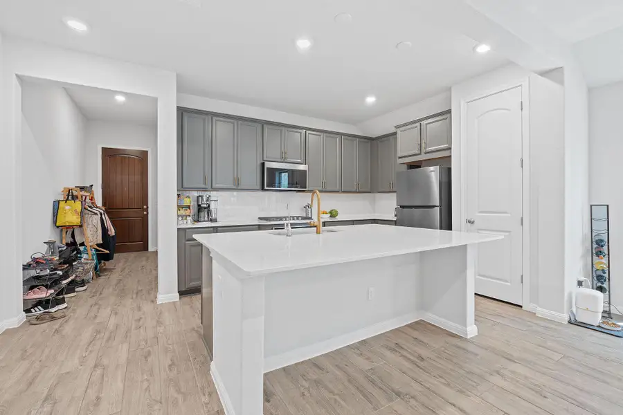 Kitchen featuring decorative backsplash, gray cabinets, light wood finished floors, stainless steel appliances, and a kitchen island with sink Kitchen featuring decorative backsplash, gray cabinets, light wood finished floors, stainless steel appliances, and a kitchen island with sink