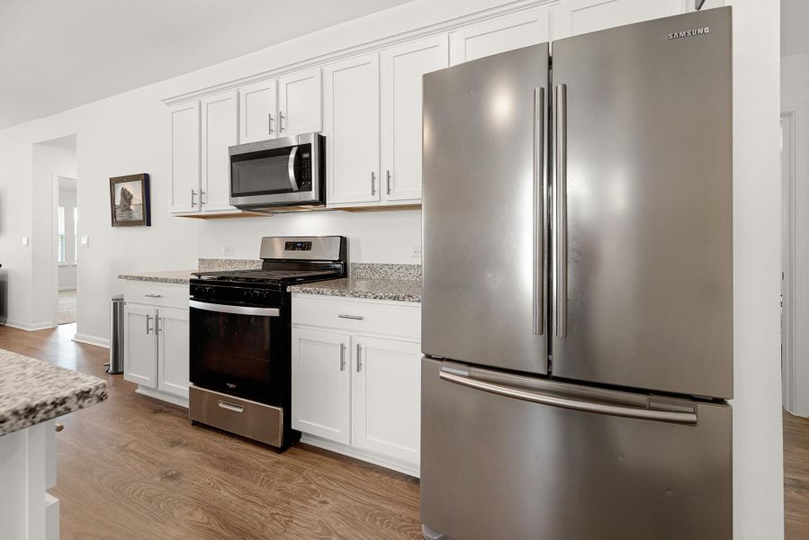 Kitchen with stainless steel appliances, white cabinetry, light stone countertops, and dark wood-type flooring