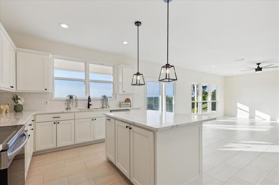 Kitchen with backsplash, light stone counters, a kitchen island, ceiling fan, and white cabinets