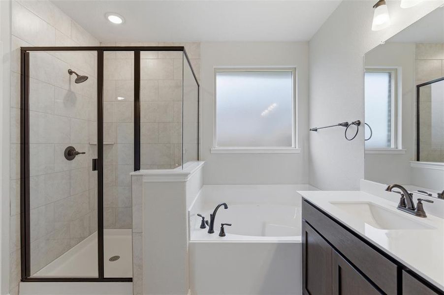 Full bathroom featuring a walk-in shower with tile surround and dark-framed glass enclosure, a built-in bathtub, a vanity with an undermount sink and dark cabinetry, and a frosted window