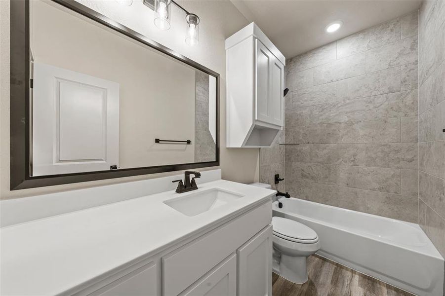 Contemporary bathroom featuring a white vanity with integrated sink, a dark framed mirror, and a combined tub and shower with light-toned tile surround Contemporary bathroom featuring a white vanity with integrated sink, a dark framed mirror, and a combined tub and shower with light-toned tile surround