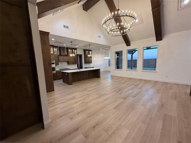 Kitchen featuring open floor plan, pendant lighting, high vaulted ceiling, an island with sink, and light wood-style flooring Kitchen featuring open floor plan, pendant lighting, high vaulted ceiling, an island with sink, and light wood-style flooring