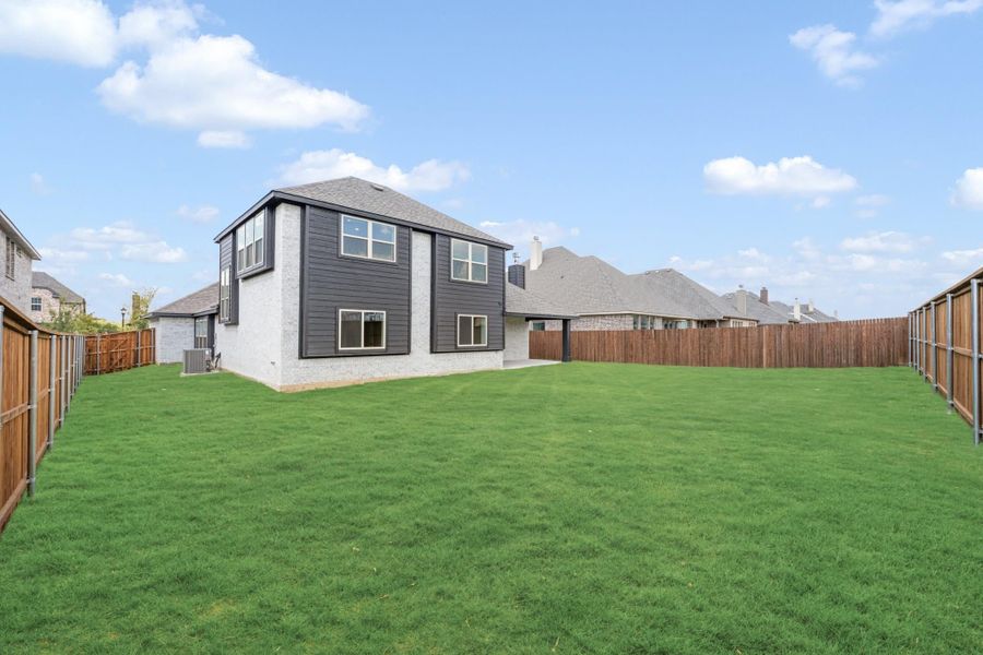 Backyard of two-story home with dark siding, large green lawn, and wood privacy fence