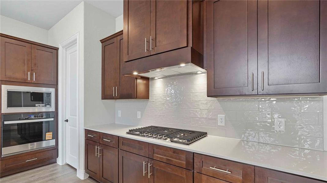 Kitchen featuring dark wood-finish cabinetry, light-toned countertops, a stainless steel gas cooktop, a built-in microwave, and a wall oven