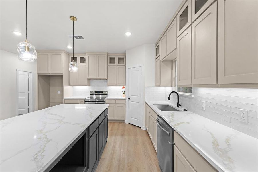 Modern kitchen featuring a large island with a white and gold veined countertop, pendant lighting, light-toned cabinetry, stainless steel appliances, and wood-finish flooring Modern kitchen featuring a large island with a white and gold veined countertop, pendant lighting, light-toned cabinetry, stainless steel appliances, and wood-finish flooring